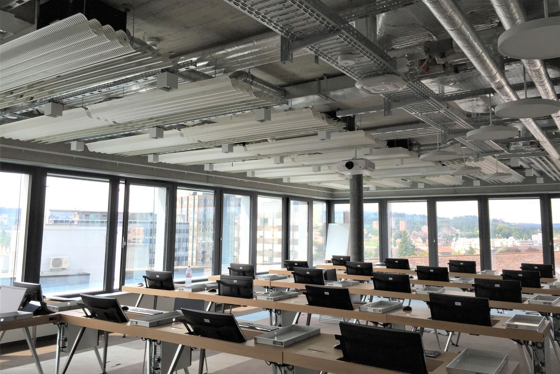 Modern classroom with rows of computers and large windows overlooking a cityscape.