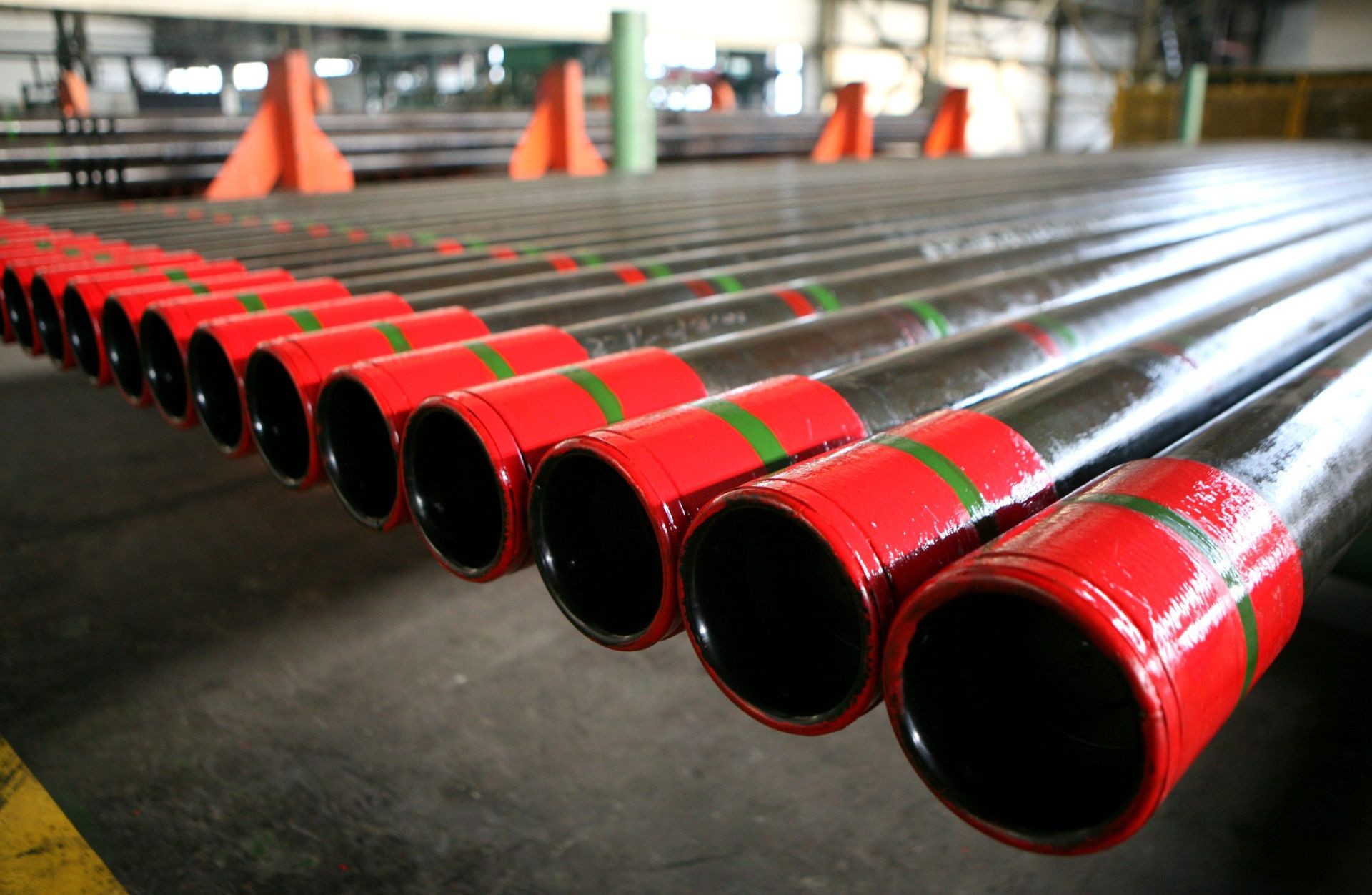 Close-up view of steel pipes with red ends arranged in a row inside an industrial warehouse.